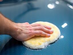 Hand applying wax to a car's hood.
